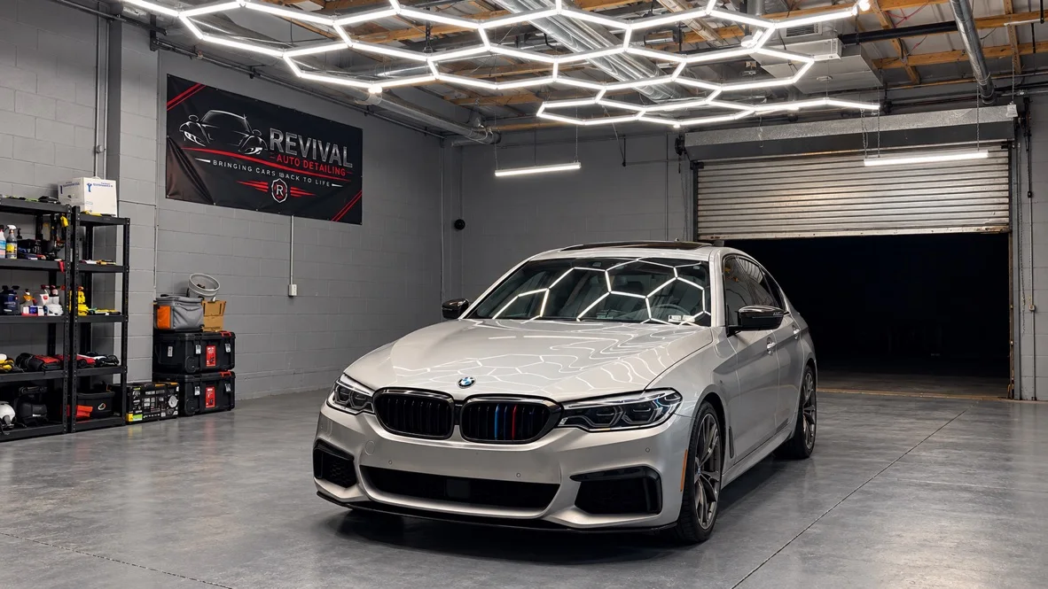 A freshly detailed BMW M550i inside the Revival Auto Detailing shop in North Wales, under hexagon lights with the Revival banner on the wall